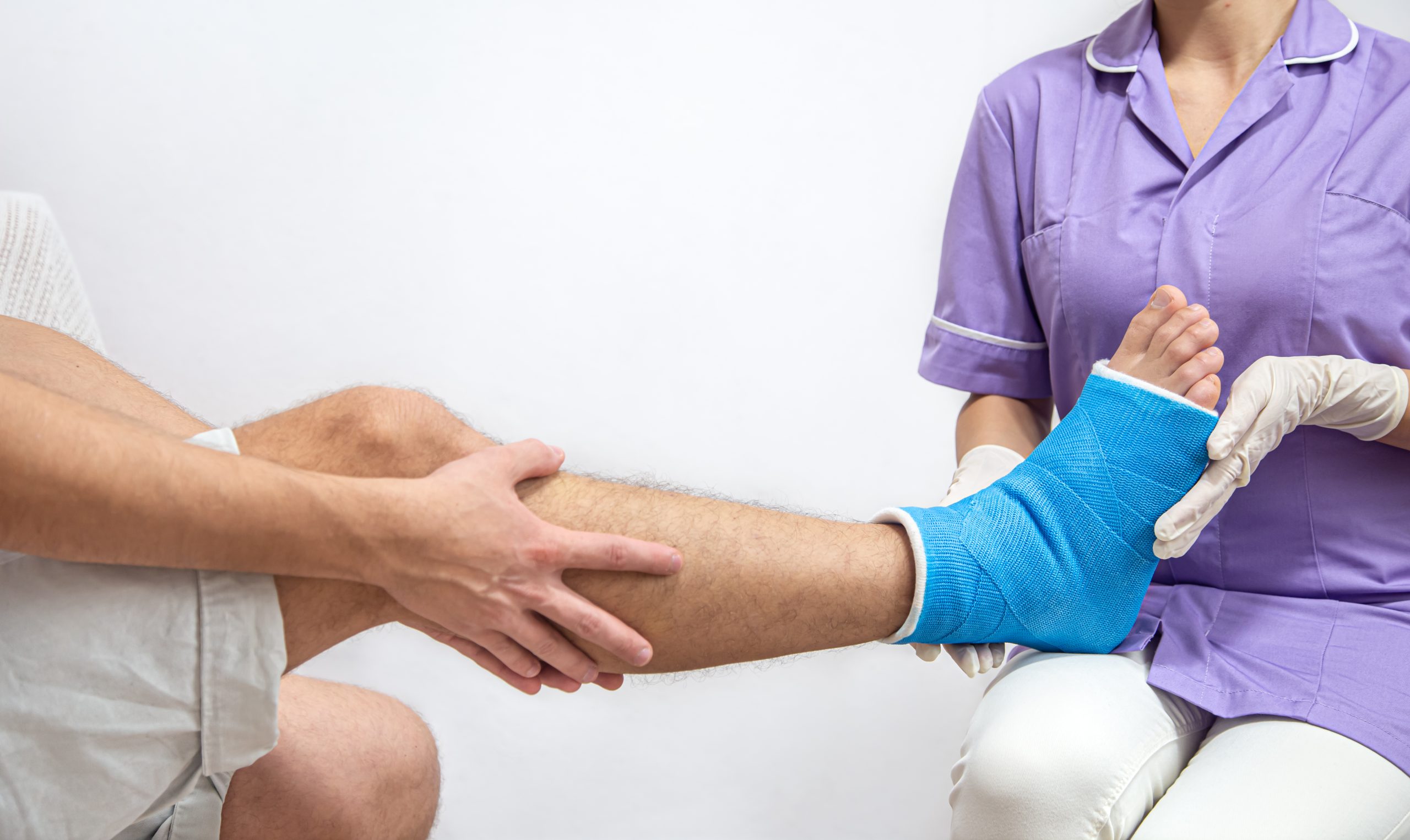 Female doctor in a blue medical gown checking broken leg on male patient.