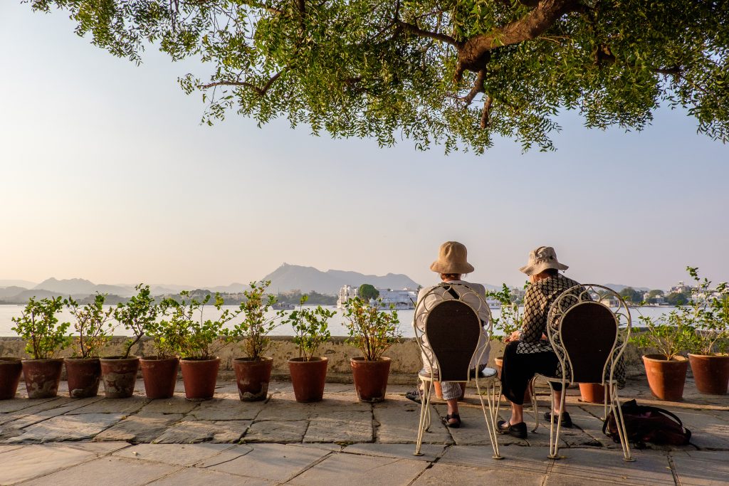 Females wearing hats sitting on chairs near flower pots looking at the mountains in the distance