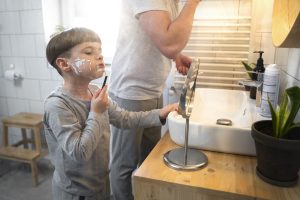 Side view kid learning shave with mirror